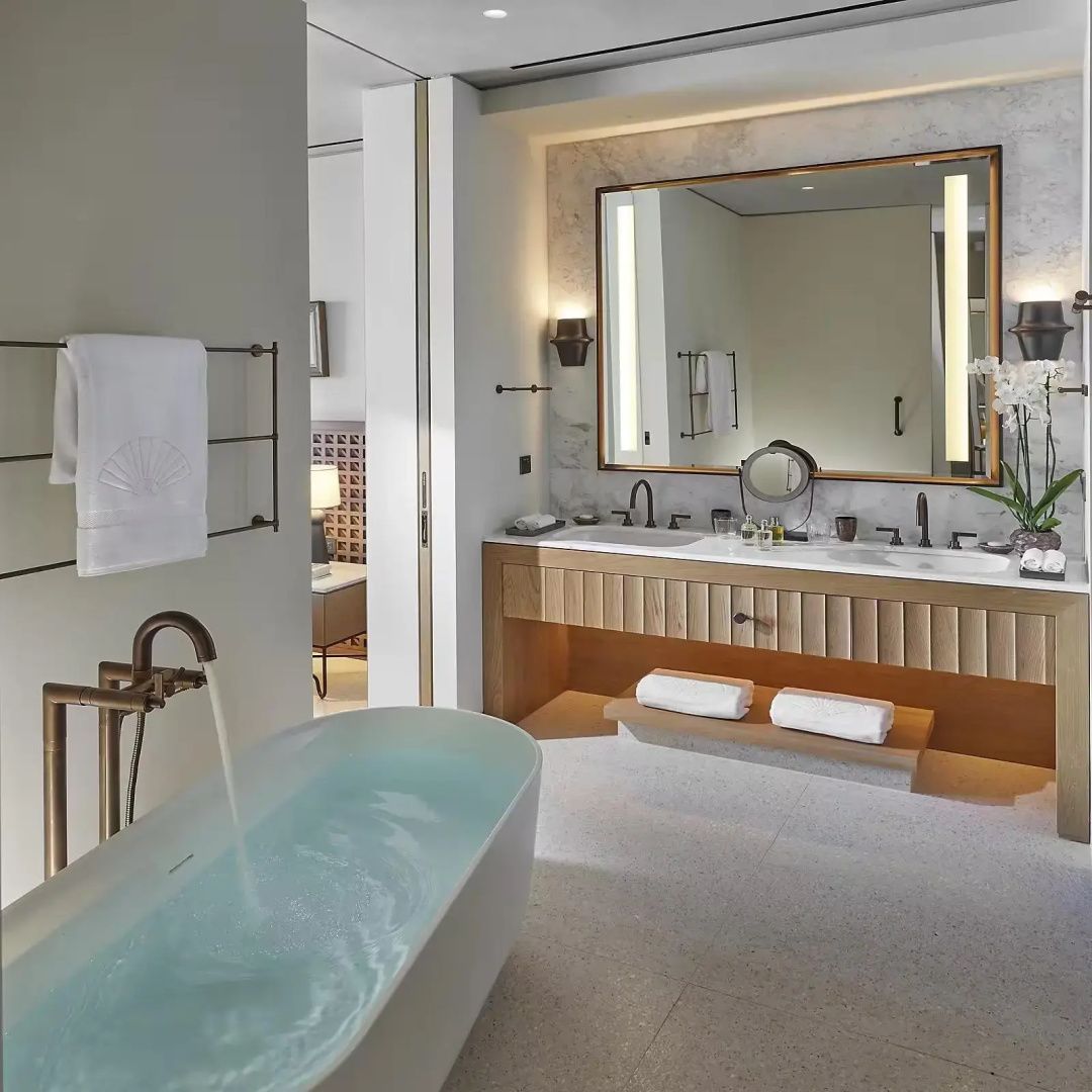 Badezimmer mit befüllter freistehender Badewanne, großem Spiegel und hölzernem Waschtisch.