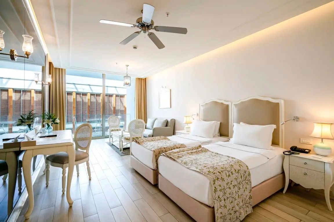 Geräumiges Hotelzimmer mit zwei Einzelbetten, Sitzecke und Deckenventilator.