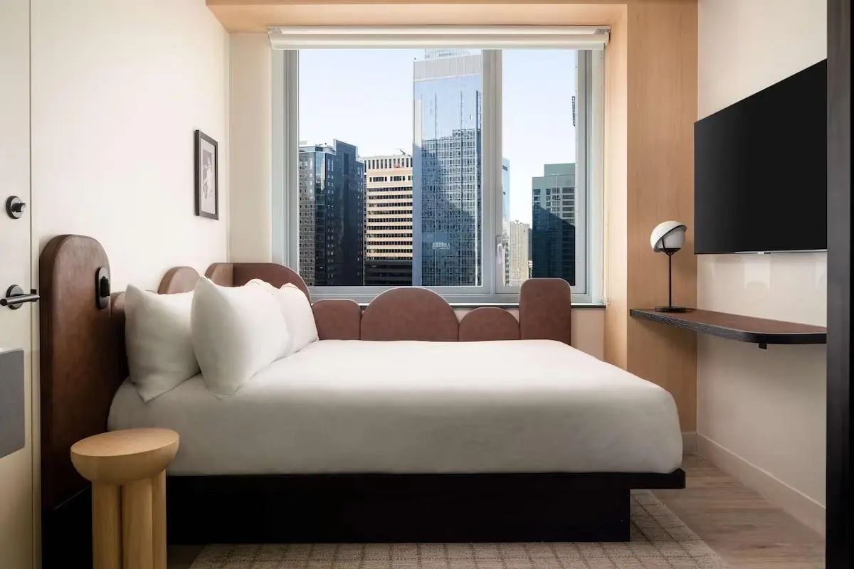 Modernes Hotelzimmer mit großem Bett und Blick durch das Fenster auf Hochhäuser in New York.