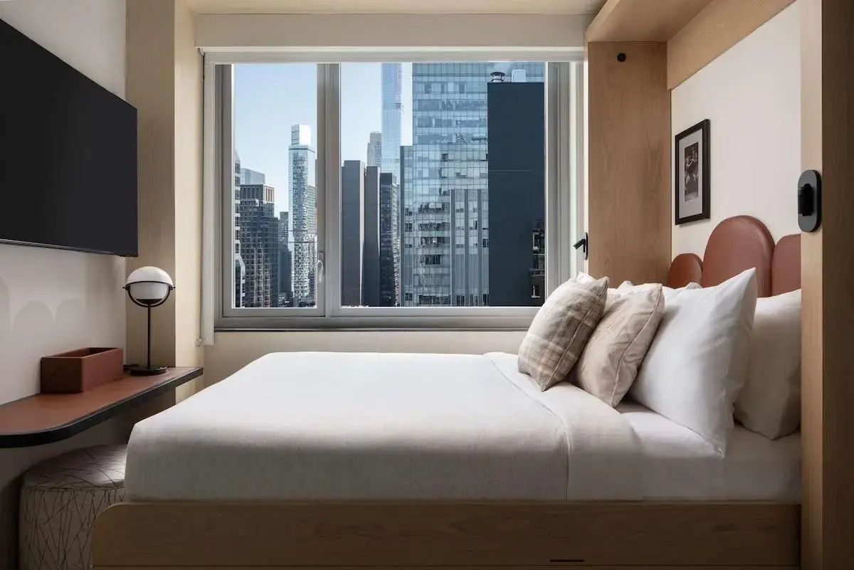 Bett mit Kissen im Hotelzimmer mit direktem Blick aus dem Fenster auf die Hochhäuser der Stadt.