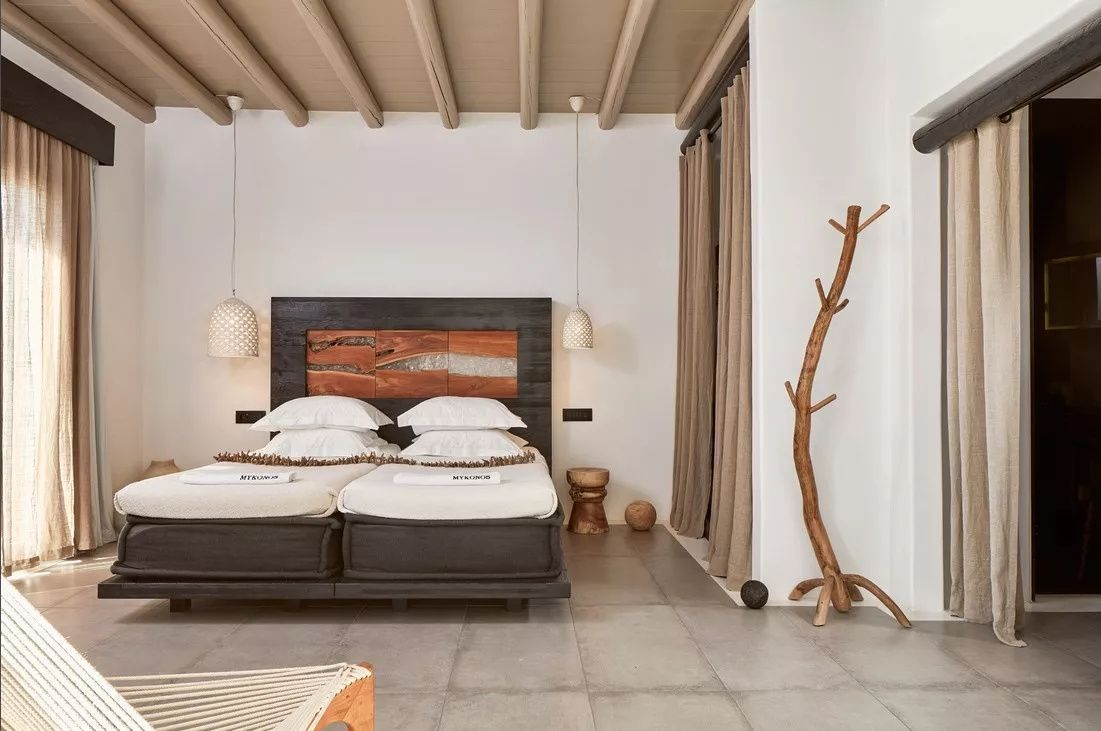 Hell eingerichtetes Schlafzimmer mit Doppelbett, hölzerner Balkendecke und Garderobenständer aus Holz.