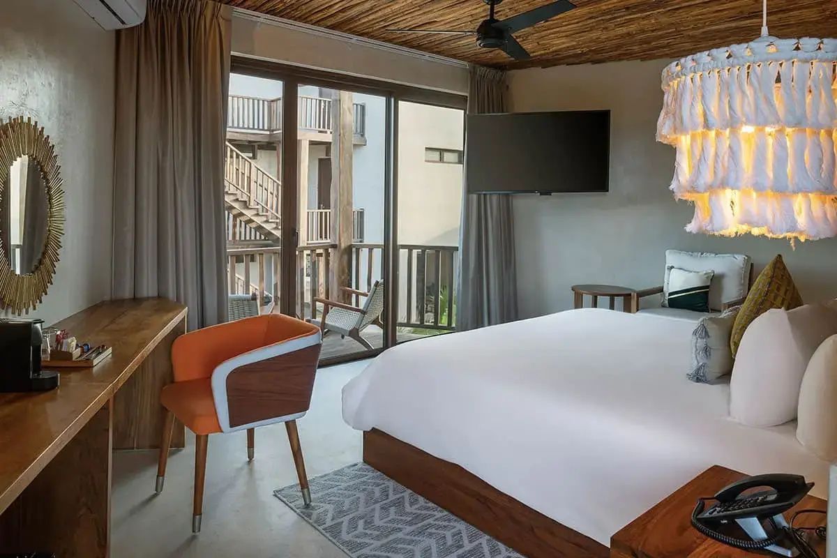 Modernes Hotelzimmer mit großem Doppelbett, orangem Sessel und Glasfront zum Balkon.