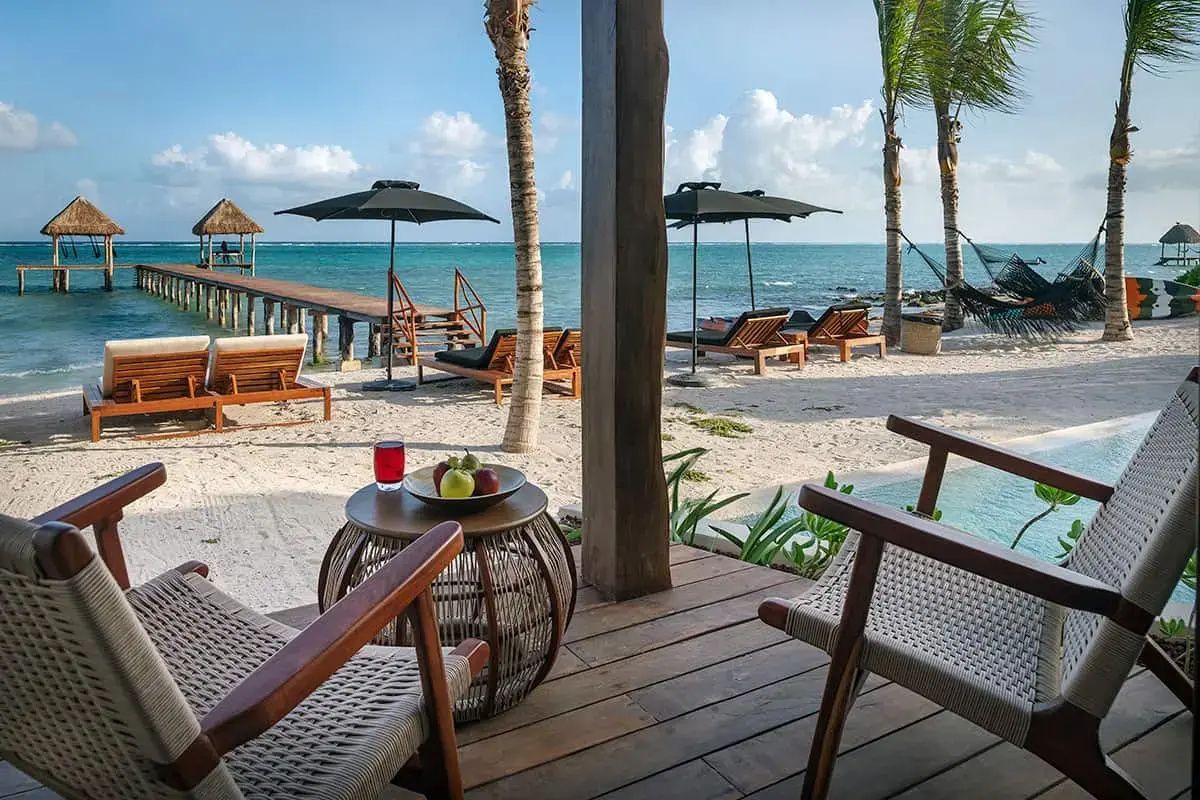 Blick von einer Holzterrasse auf den Sandstrand mit Sonnenschirmen, Palmen und Holzkai.
