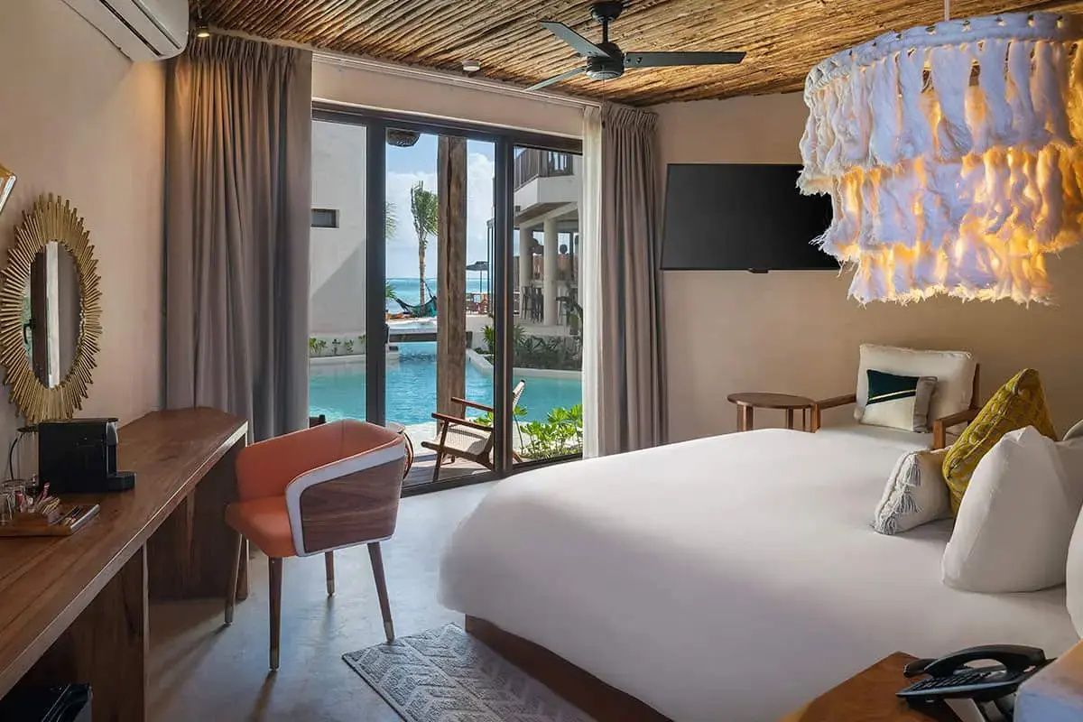 Modernes Hotelzimmer mit Kingsize-Bett, Sitzbereich und Blick durch die Glasfront auf den Pool.