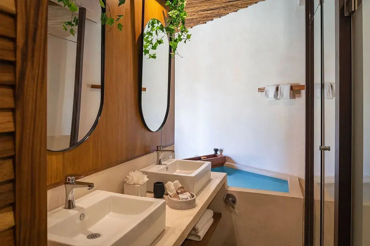 Badezimmer mit zwei Waschbecken, ovalen Spiegeln und einer blau gefliesten Badewanne.