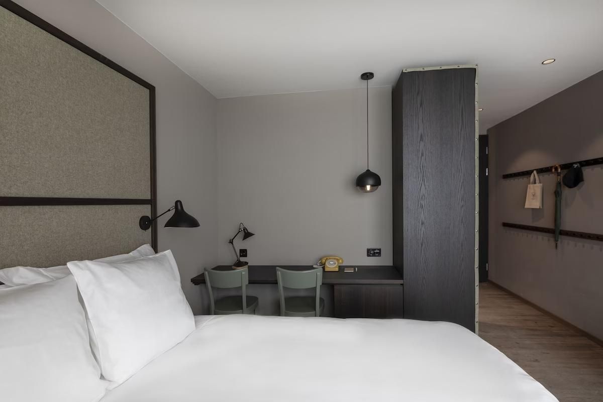 Modern eingerichtetes Hotelzimmer mit weißem Bett, Schreibtisch und dunklem Schrank.