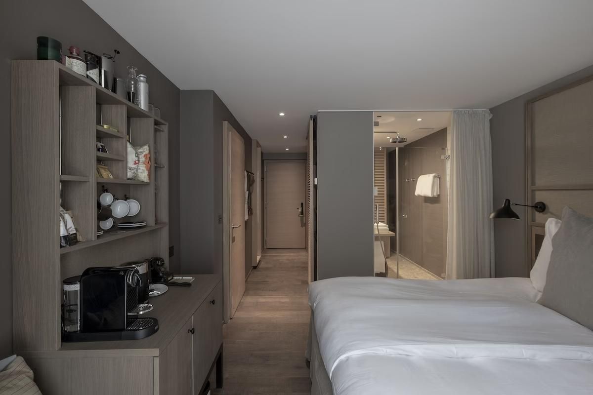 Blick durch das moderne Hotelzimmer mit Bett, Minibar und gläsernem Bad.