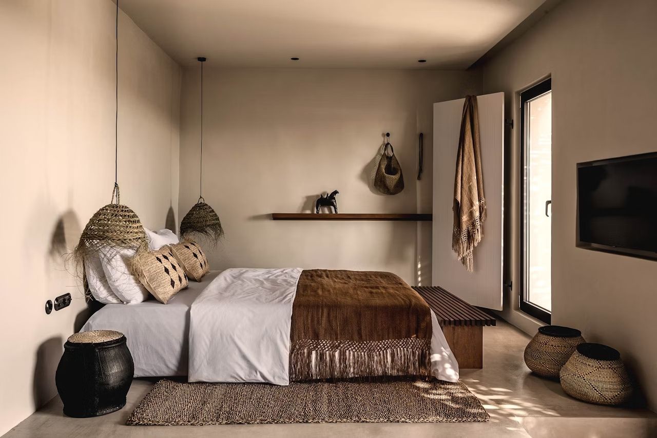 Doppelbett mit weißer Bettwäsche, brauner Tagesdecke und Lampen aus Naturmaterialien.