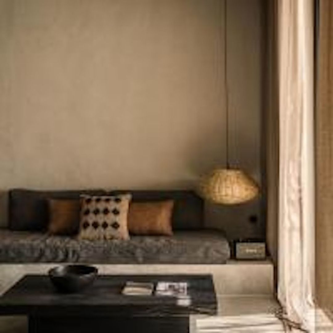 Sitzbereich mit niedrigem Sofa, dunklem Holztisch und einer geflochtenen Hängelampe.