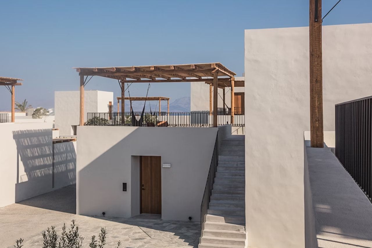 Weißes Hotelgebäude mit Außentreppe, Holztür und Pergola auf der Dachterrasse.