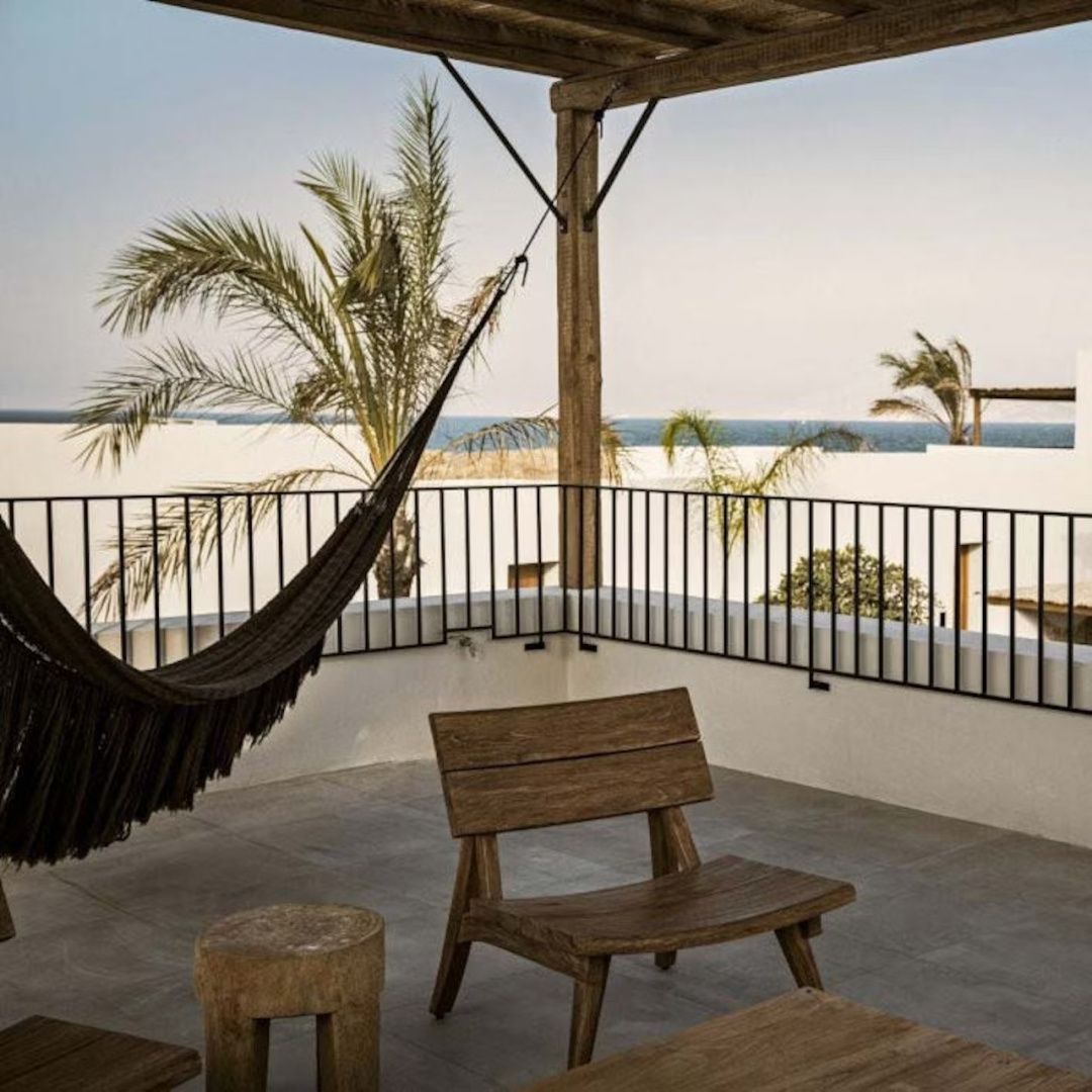 Terrasse mit Holzstuhl, schwarzer Hängematte und Blick über Palmen auf das Meer.