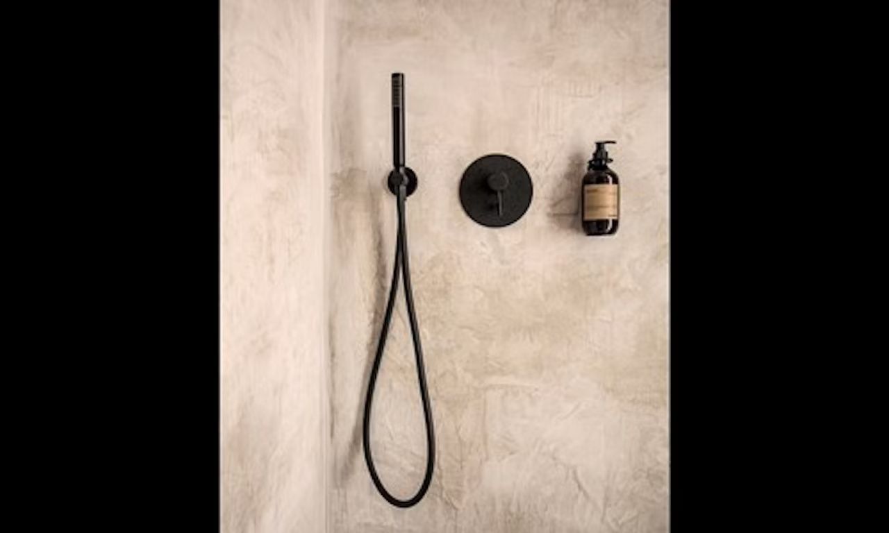 Schwarze Duscharmatur und ein Seifenspender an einer hellen Wand im Badezimmer.