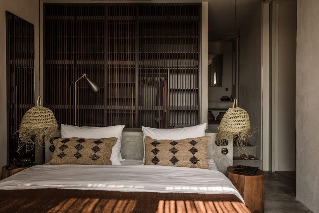 Doppelbett mit Kissen im Boho-Stil und einer dunklen Holzwand dahinter.