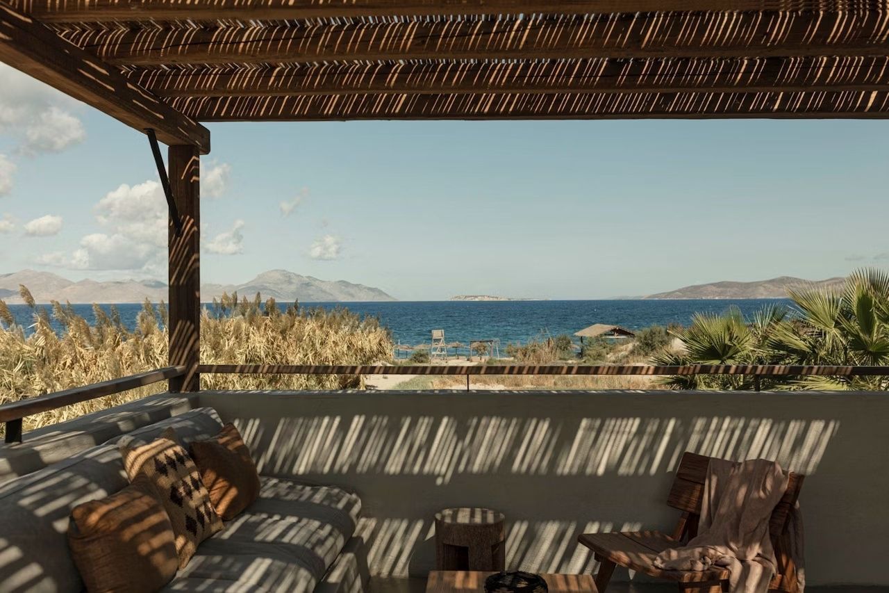 Blick von einer überdachten Terrasse auf das blaue Meer und entfernte Inseln.