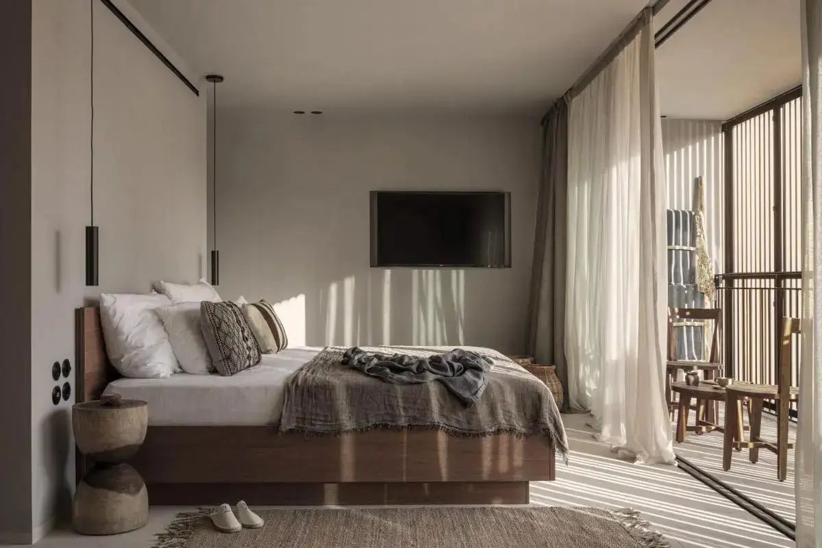 Helles Schlafzimmer mit Holzdoppelbett, Flachbildfernseher an der Wand und Vorhängen.