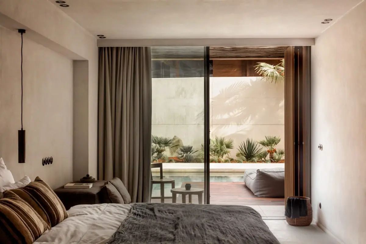 Blick aus dem Schlafzimmer auf eine private Terrasse mit Pool und Palmen im Außenbereich.