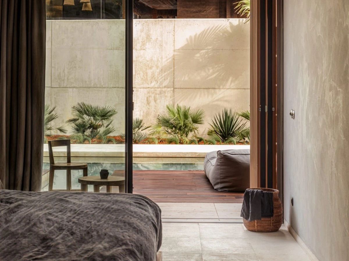 Ausblick durch eine geöffnete Glasfensterfront auf die Holzterrasse mit Pool und Pflanzen.