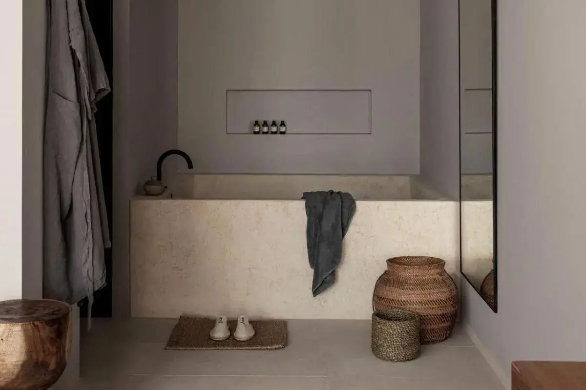 Badewanne aus hellem Stein mit aufgelegtem Handtuch, Pantoffeln und zwei Flechtkörben.
