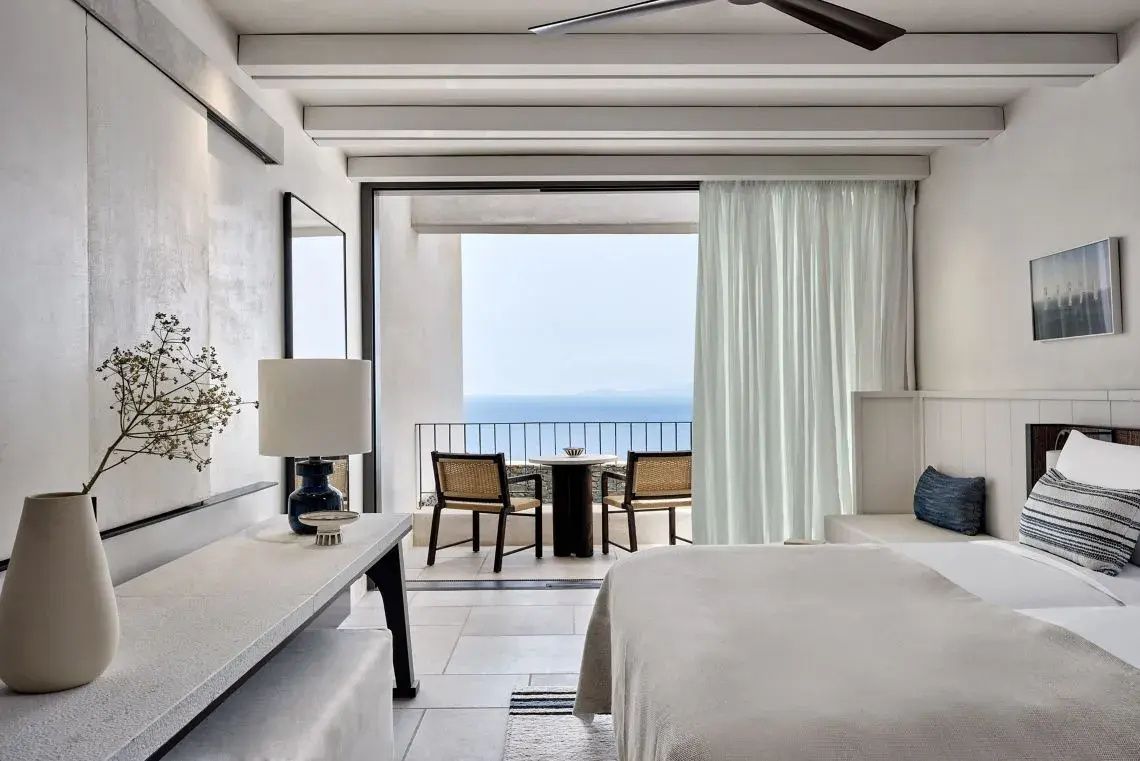 Schlafzimmer mit großem Fenster und Balkon mit Sitzgelegenheit und Meerblick.