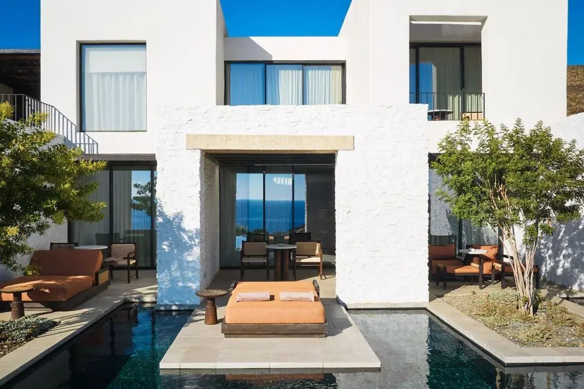 Weiße Fassade einer Suite mit Private Pool, Liegebett und Blick auf das blaue Meer.