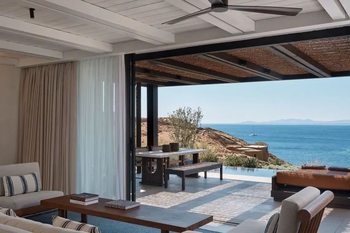 Blick von einem hellen Wohnbereich über die überdachte Terrasse mit Esstisch auf den Pool und das Meer.