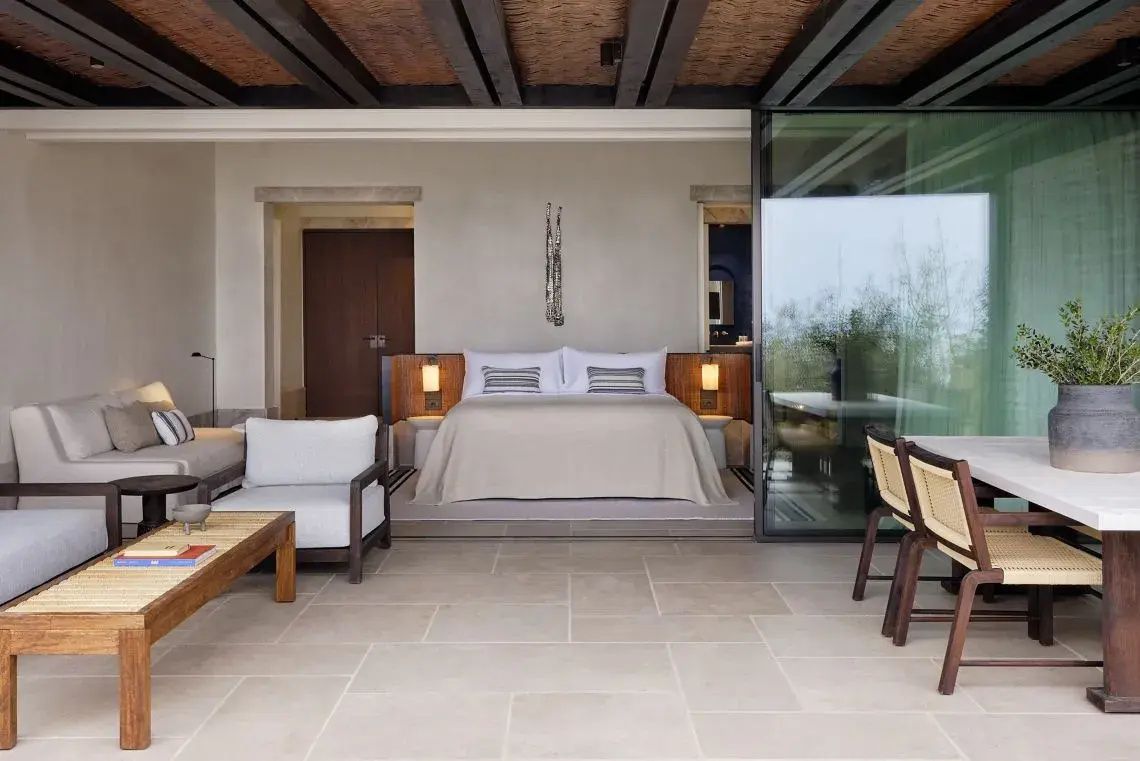 Modern eingerichtetes Hotelzimmer mit einem Doppelbett, Holzbalkendecke und hellen Sesseln.