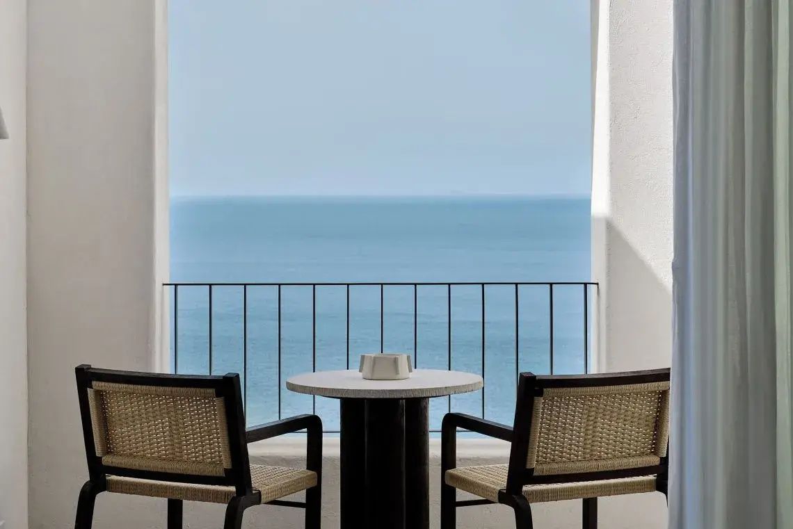 Balkon mit zwei Flechtstühlen und einem kleinen Tisch direkt am blauen Meer.