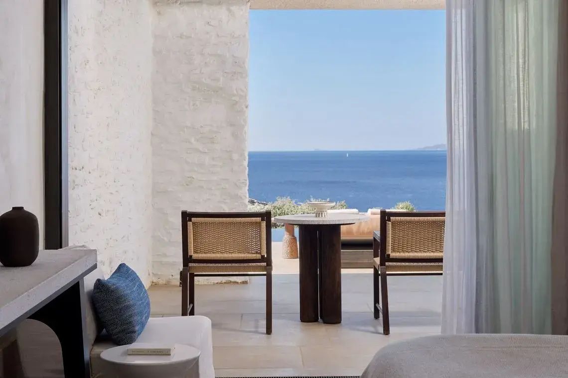 Sitzgruppe aus Holz und Geflecht auf der Terrasse mit direkter Sicht auf das blaue Meer.