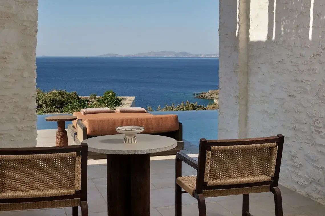 Terrasse mit Esstisch, Stühlen und Sonnenliege vor einem Pool mit Meerblick.
