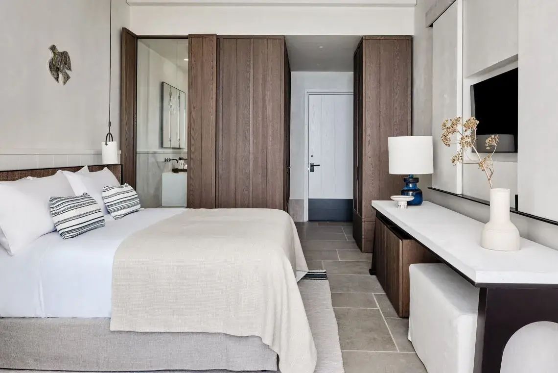 Hotelzimmer mit weiß bezogenem Bett, dunklen Holzschränken und hellen Fliesen.