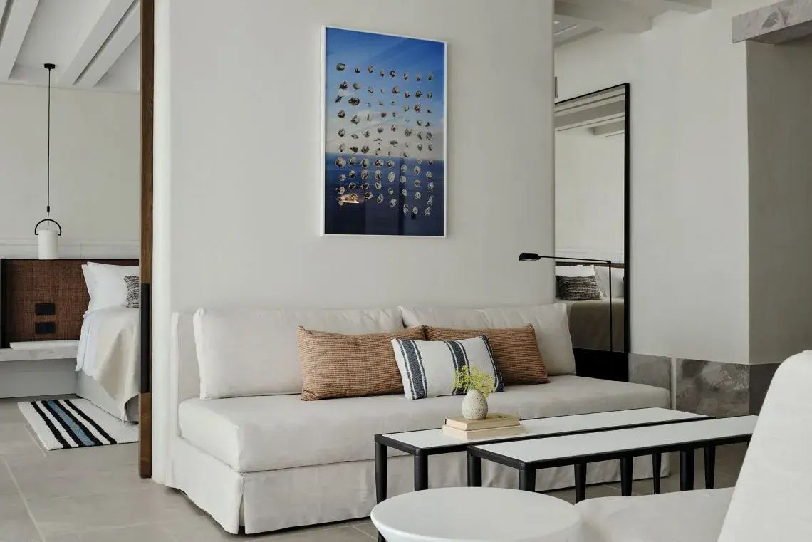 Sitzbereich mit beigem Sofa, Kissen, zwei kleinen Tischen und einem Kunstwerk an der Wand.