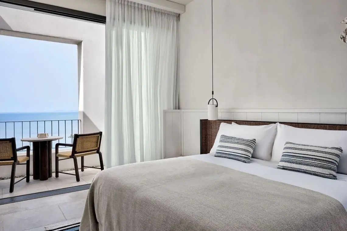 Helles Hotelzimmer mit großem Bett, beigen Stoffen und Zugang zum Balkon.