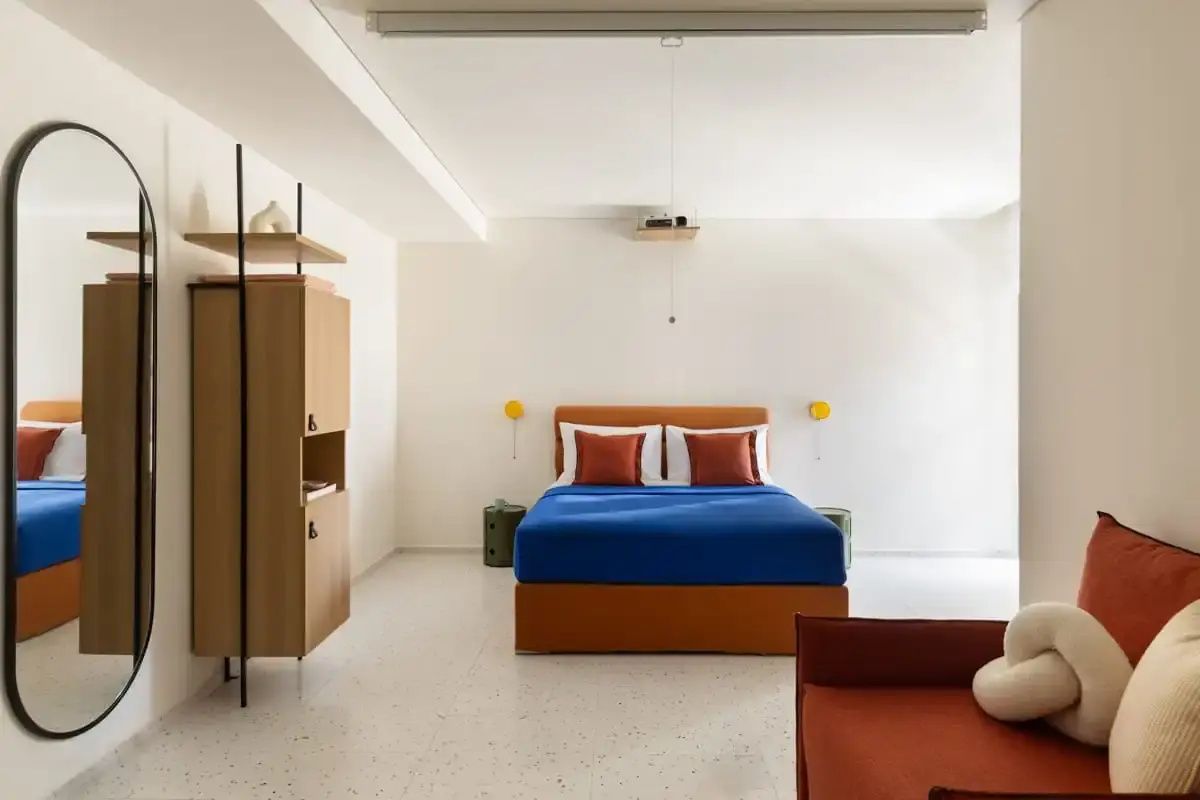 Hell gestaltetes Hotelzimmer mit blauem Doppelbett und Holzschrank