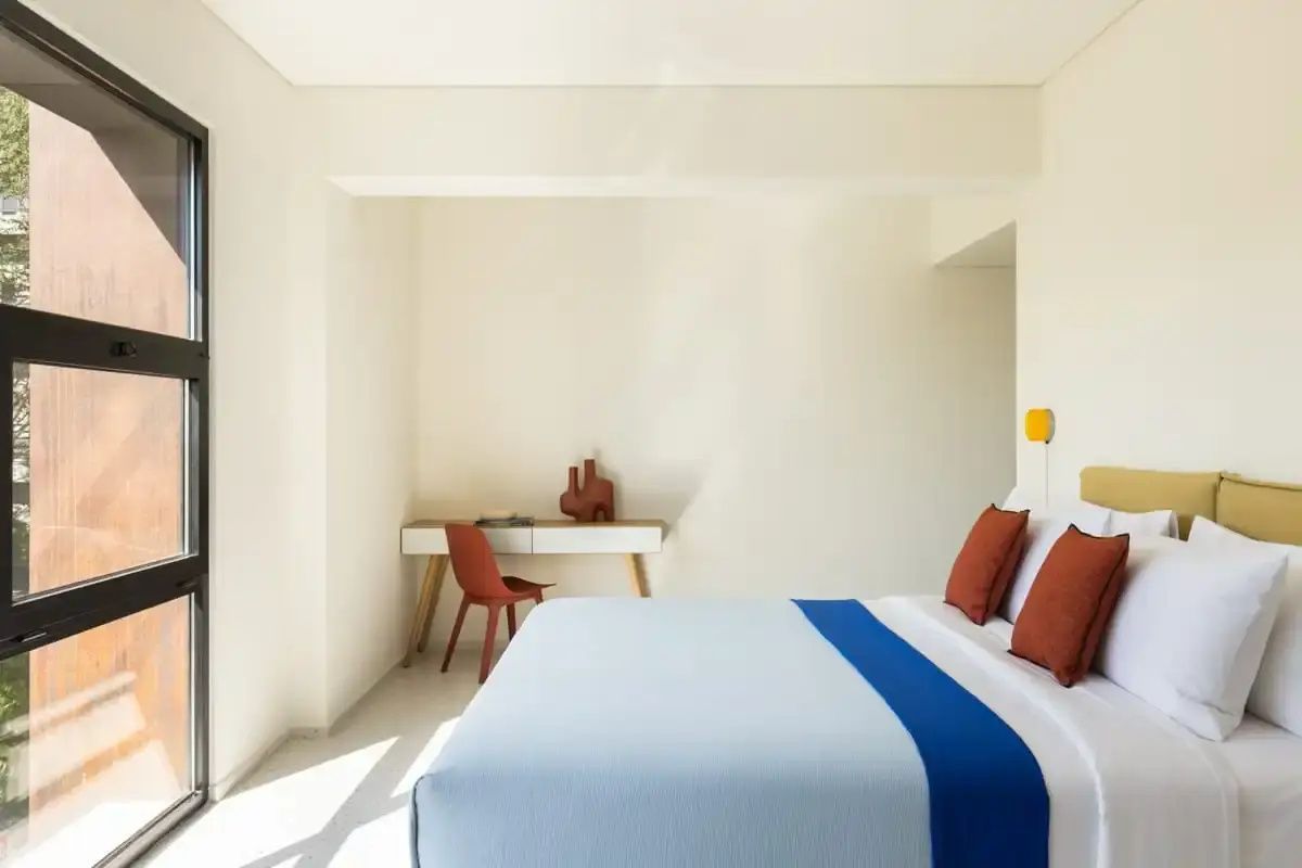 Minimalistisches Zimmer mit hellem Bett, rotem Stuhl und Schreibtisch in einer hellen Nische.