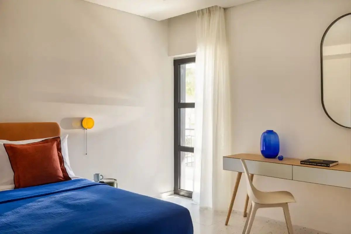 Schlafbereich im Hotelzimmer mit Schreibtisch, blauer Vase und Fenster