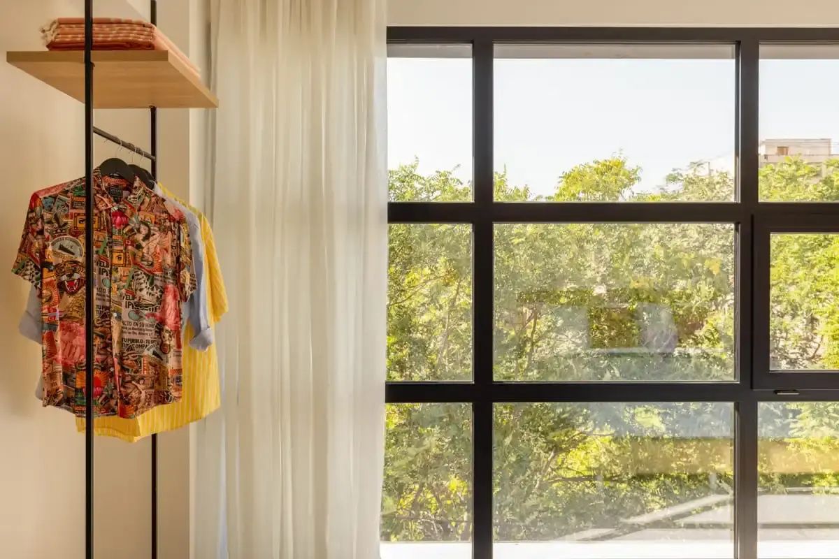 Großes Fenster mit Blick ins Grüne neben einem Kleiderständer mit Kleidung.