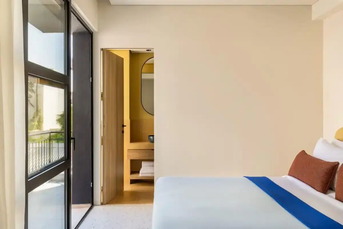 Hotelzimmer mit Bett, großem Balkonzugang und Durchgang zum gelb gefliesten Badezimmer.