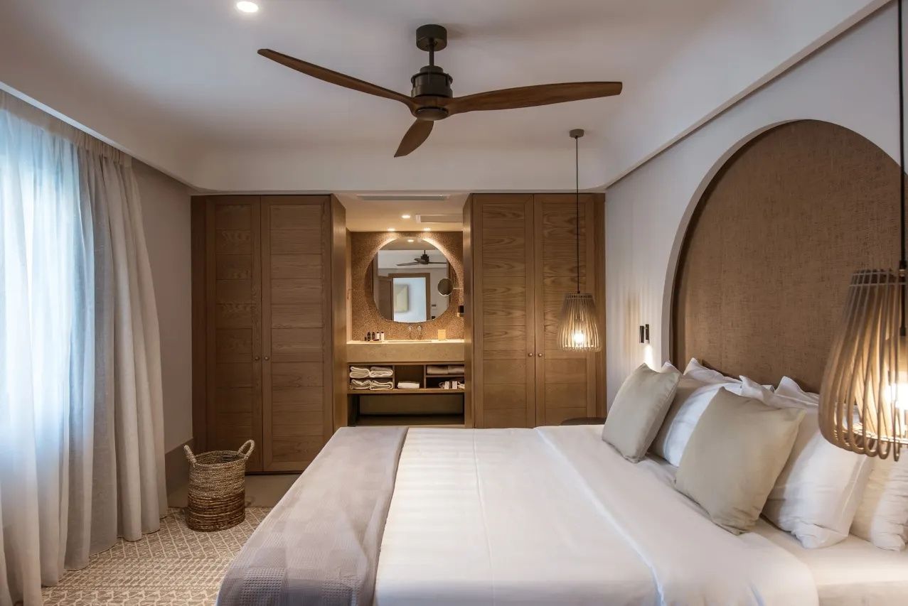 Doppelbett in hellem Hotelzimmer mit Holzschränken und Deckenventilator.