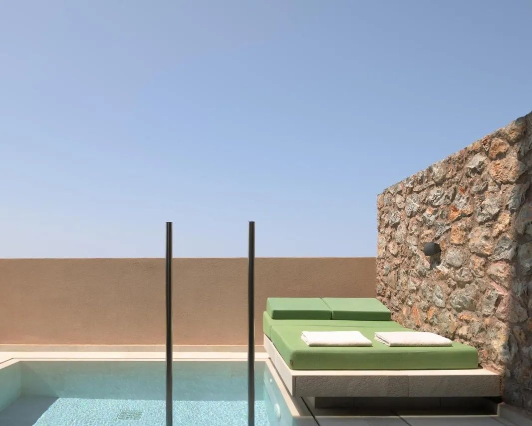 Sonnendeck mit grüner Liegefläche an einem privaten Pool vor einer Natursteinwand.
