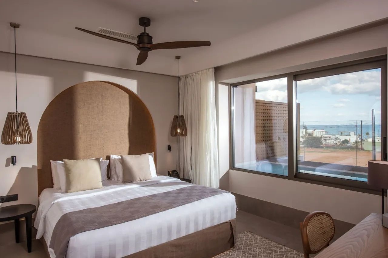 Modernes Hotelzimmer mit Doppelbett, Ventilator an der Decke und Blick nach draußen.