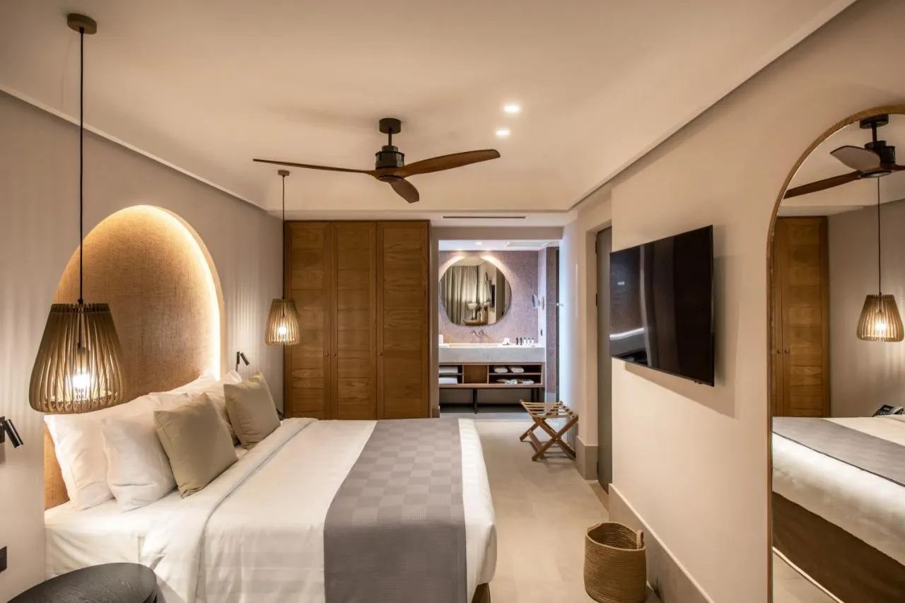 Schlafzimmer im hellen Design mit Fernseher an der Wand, Holzschrank und integriertem Bad.