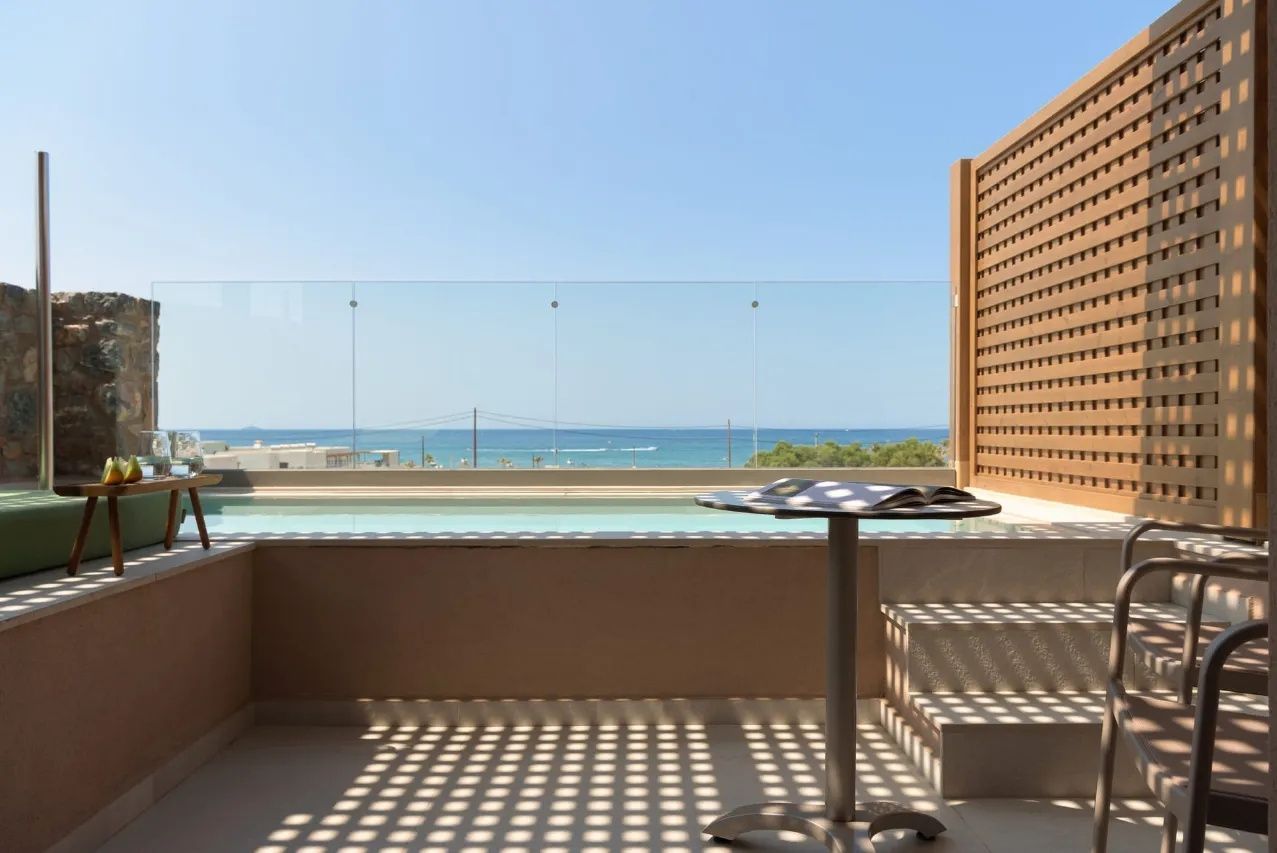 Blick von der Terrasse über ein Geländer aus Glas auf das blaue Meer.