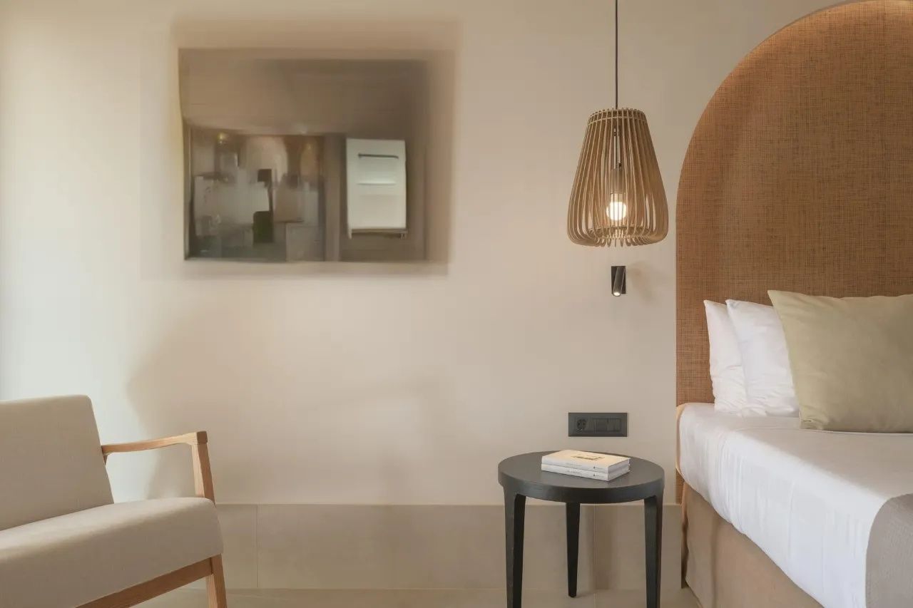 Nachttisch aus Holz neben dem Bett mit Pendelleuchte und Sessel an der Wand.