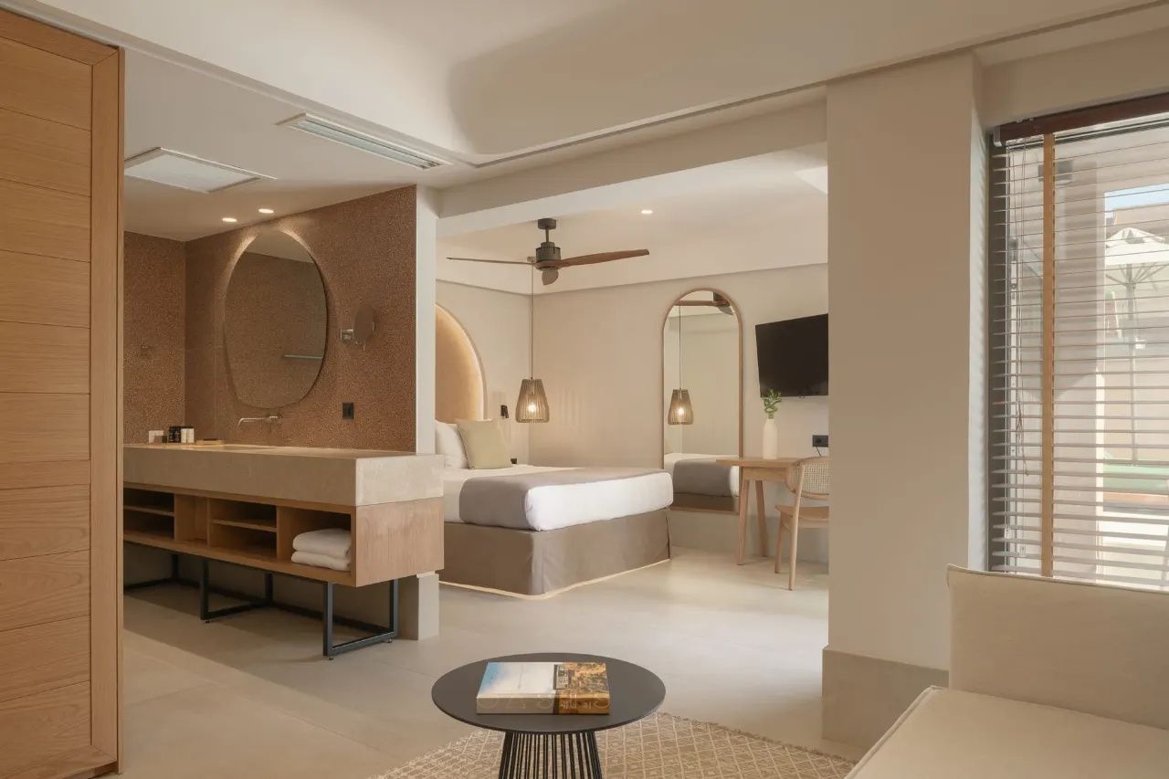 Helles Hotelzimmer mit Sitzbereich im Vordergrund und Doppelbett dahinter.