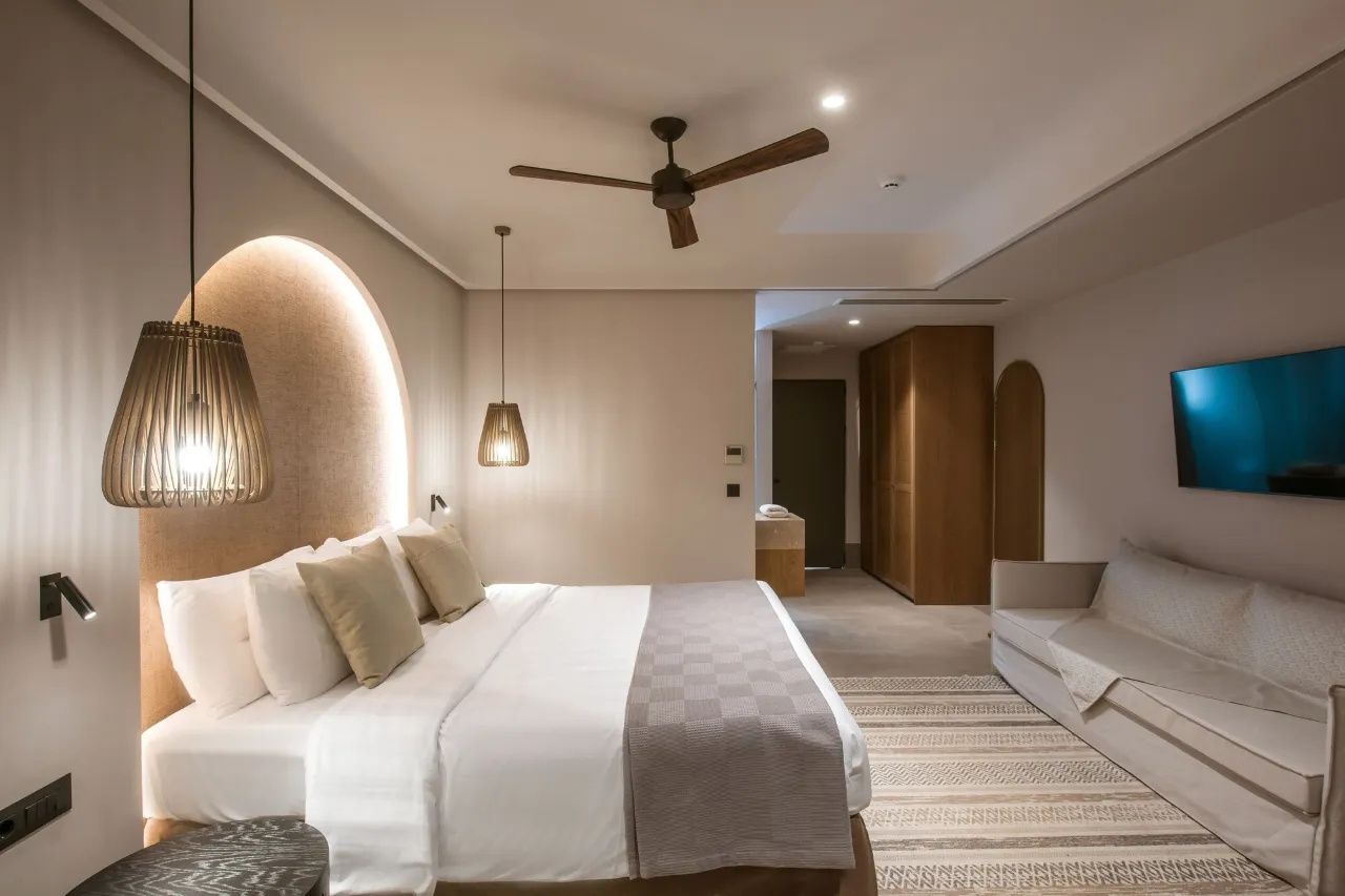 Großes Doppelbett und Sofa im hell eingerichteten Hotelzimmer mit Holzschrank