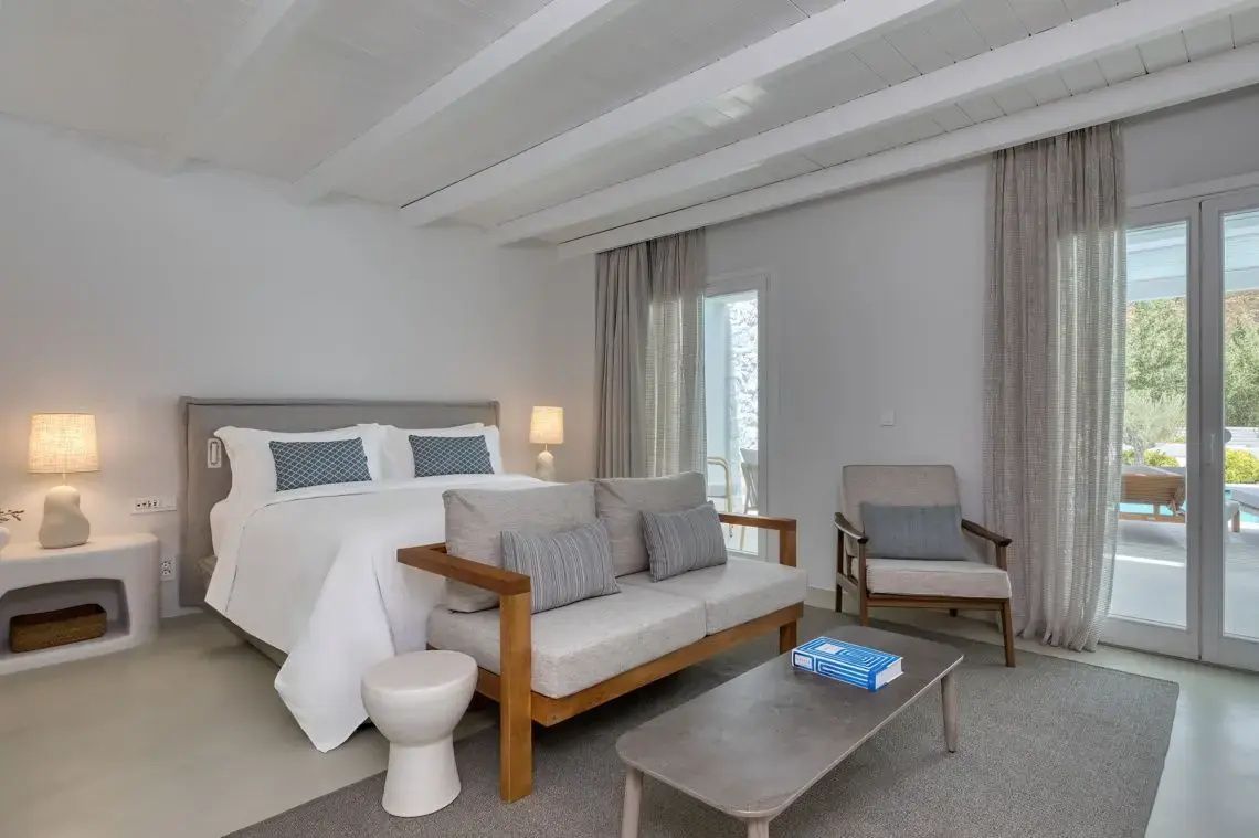 Hell eingerichtetes Schlafzimmer mit weißem Doppelbett, Sofa und Couchtisch.