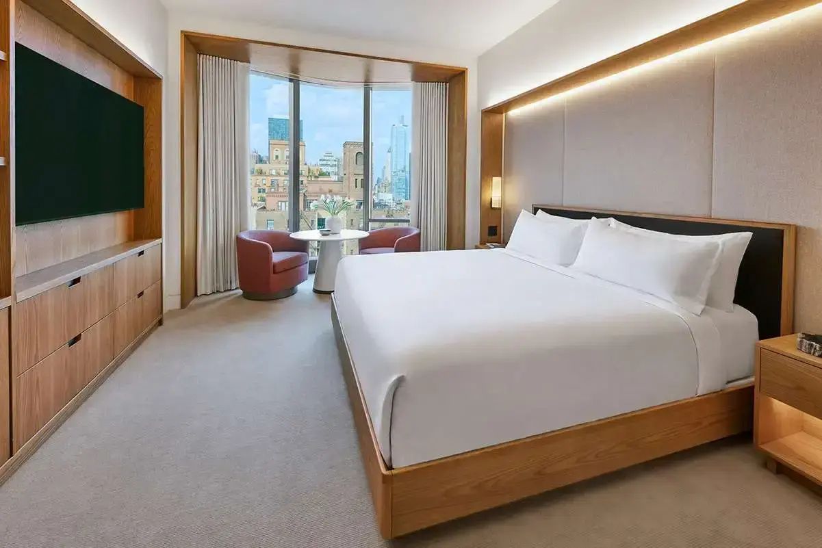 Hotelzimmer mit großem Doppelbett, Holzverkleidungen und Sitzbereich vor einem Fenster mit Stadtblick.