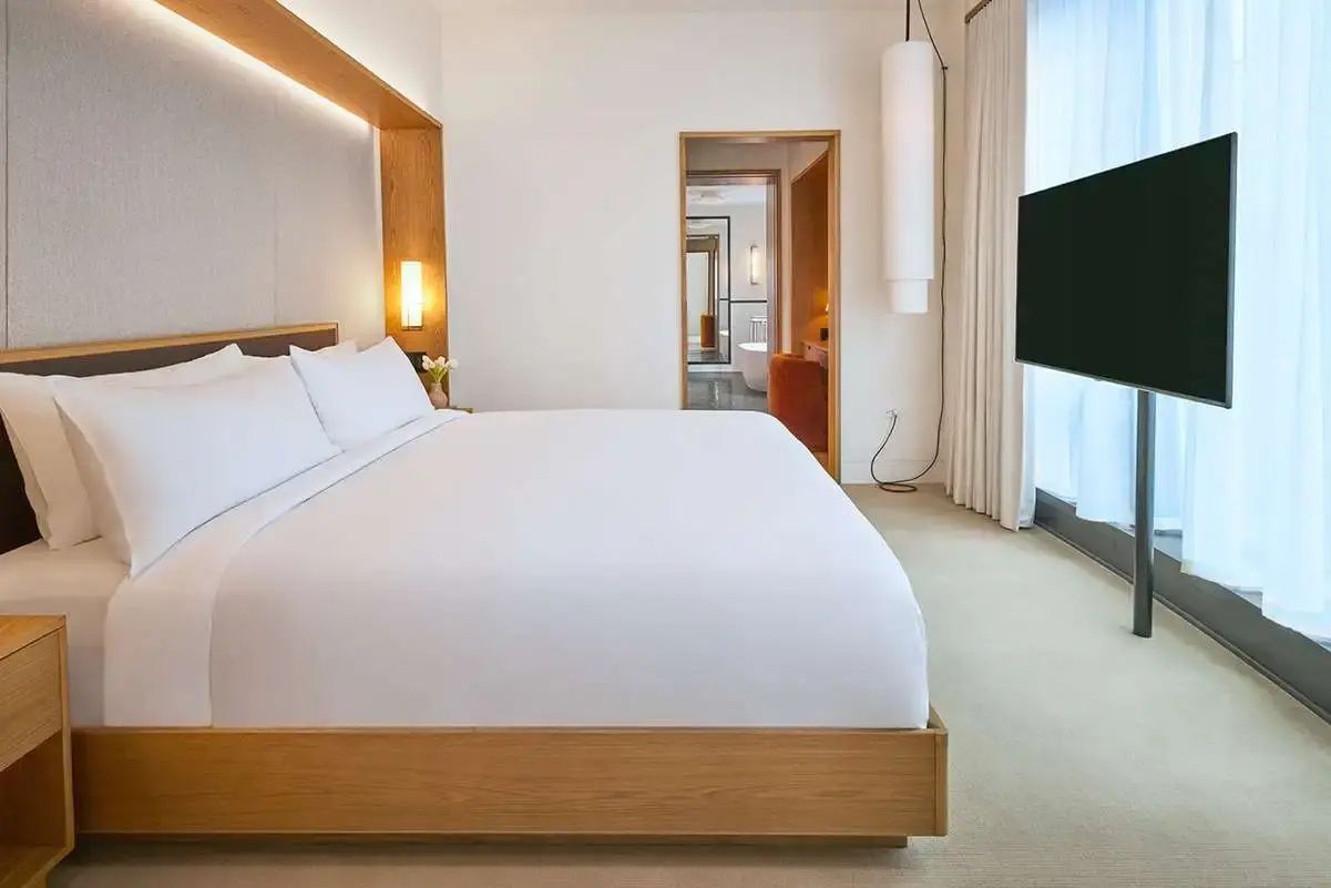 Schlafbereich mit großem Doppelbett, Holzrahmen, weißer Bettwäsche und Blick in den Flur.