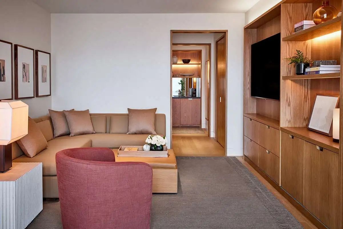 Wohnzimmer einer Hotel Suite mit hellem Ecksofa, rotem Sessel und Flachbildfernseher.