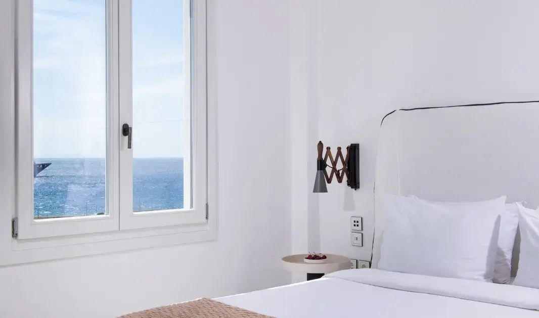 Nachttisch mit Wandleuchte und Fenster mit Blick auf das offene Meer.